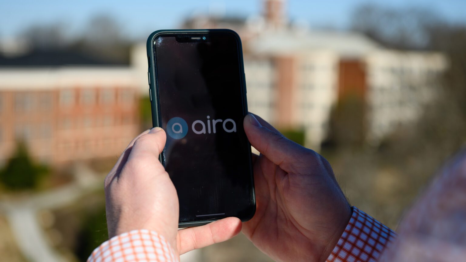 Person holding a smartphone with the Aira logo on the screen.